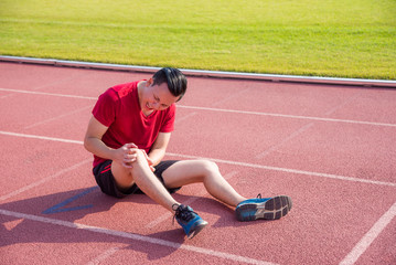 Young asian runner having pain at knee between running in stadium