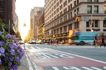  New York City-tourbus rijdt over 5th Avenue in Manhattan met mensen die door de kruising lopen en de zonsondergang op de achtergrond © deberarr