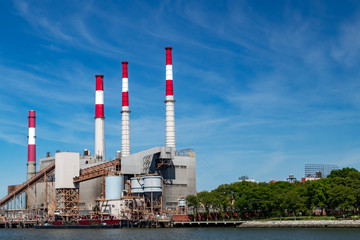 Power plant smoke stack towers contrast against blue sky background and green trees below