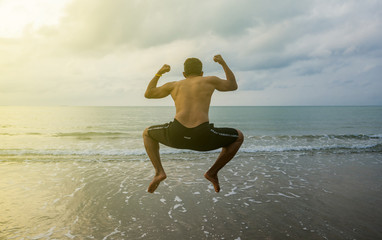 Back view of relax man jump to the sea.Smart man enjoy jumping on the beach at sunrise time.