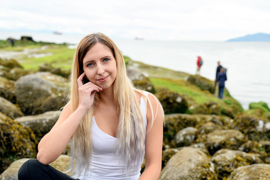 Young woman sitting on rock and smiling friendly into the camera in the intertidal zone of Vancouver, British Columbia