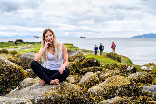 Young woman sitting on rock and smiling friendly into the camera in the intertidal zone of Vancouver, British Columbia