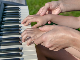 Mother teaches the daughter to play the piano. Concept Mother's Day. Female and children's hands.