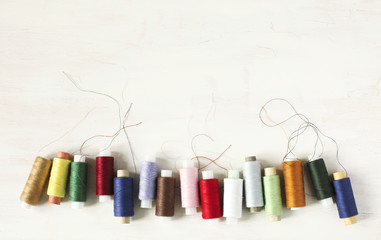 Colourful thread spools on a white wooden background with copy space