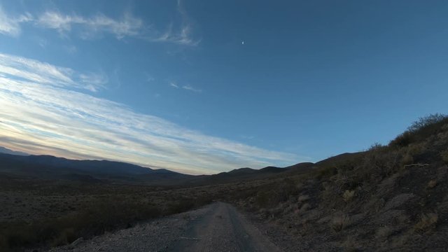 Stabilized camera movement gripped on a car at sunset golden hour. The Andes mountains on background. Van descending from mountains. Small shrubs on the sides of the gravel road. Mendoza, Argentina.