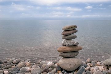 Fototapeta na wymiar Landscape, sea, sky, rocky beach and pyramid of flat gray stones.