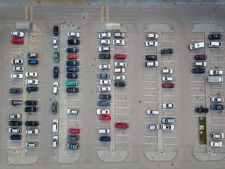 Aerial view of a large number of cars of different brands and colors standing in a parking lot near the shopping center in a chaotic manner. Parking divided by white dividing strips and sidewalks