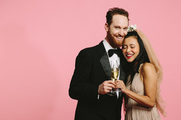 A smiling portrait of a bride and groom toasting with champagne glasses, isolated on pink - Powered by Adobe