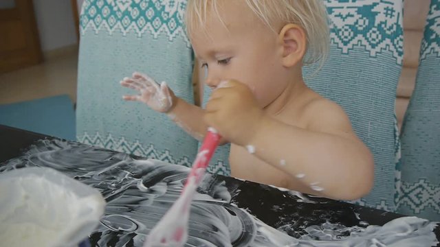 Baby eating yogurt making a mess. Cute baby girl smearing yogurt on the black glass table with spoon and palm