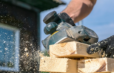 man planing boards with electric tools, chips flying in all directions. Construction, wood processing