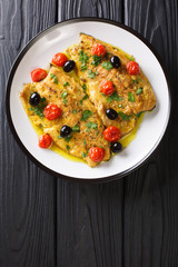 Fried trout fillets with garlic butter sauce, tomatoes and olives closeup. Vertical top view