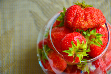 Red ripe strawberry with green leaves in a transparent glass vase in the shape of a ball on a beige background