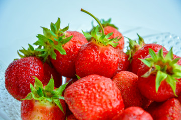 Red ripe strawberry with green leaves in a transparent glass plate on a light background