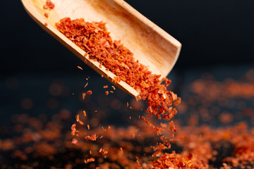 Spice red, ground, sharp bitter pepper is pouring out, a shovel is flying from a wooden scoop. Dark background