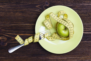 Diet concept represented by fresh green apple on plate with yellow measuring tape knotted around...