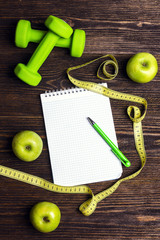 Open blank notepad with green dumbbells and green apples with measuring tape and copy space on...