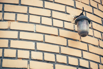 Retro street lamp on beige brick wall of building close up with copy space. Imperfect rounded brickwork with vintage streetlight.