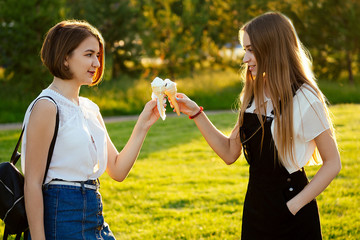 two beautifu best girlfriends schoolgirls ( student) eating ice cream in a waffle horn in the park