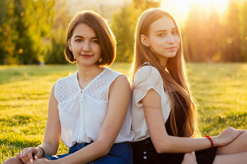 two beautifu best girlfriends schoolgirls ( student) sitting on grass in the park