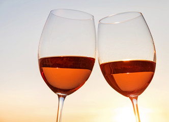 Two wine glasses on the sky background at sunset light.