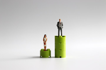 A miniature man and a miniature woman standing on a different height block.