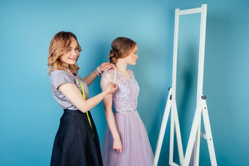 seamstress woman and bride discuss the details of wedding dress in the studio on a blue background . tailor dressmaker and customer prom in the dressing room