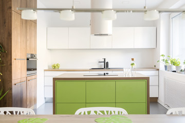 Modern and design scandinavian space with kitchen island, table and accessories. Sunny and bright kitchen with white white wall. Stylish accessories.