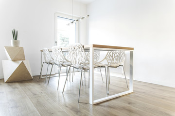 Modern scandinavian dining room with wooden table, geometric shapes, design chairs and lamp. Stylish space with white walls.
