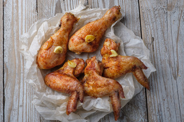 Baked chicken legs and wings lie on the table. Nearby are cherry tomatoes, celery, parsley and spices.