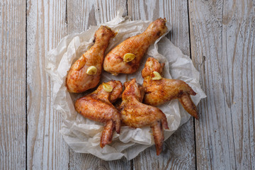 Baked chicken legs and wings lie on the table. Nearby are cherry tomatoes, celery, parsley and spices.