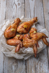 Baked chicken legs and wings lie on the table. Nearby are cherry tomatoes, celery, parsley and spices.