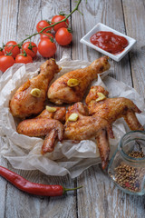 Baked chicken legs and wings lie on the table. Nearby are cherry tomatoes, celery, parsley and spices.