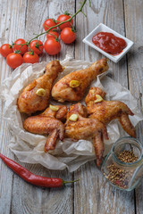 Baked chicken legs and wings lie on the table. Nearby are cherry tomatoes, celery, parsley and spices.