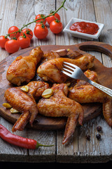 Baked chicken legs and wings lie on the table. Nearby are cherry tomatoes, celery, parsley and spices.