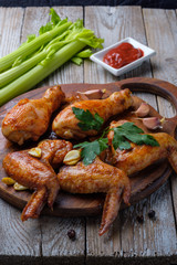 Baked chicken legs and wings lie on the table. Nearby are cherry tomatoes, celery, parsley and spices.