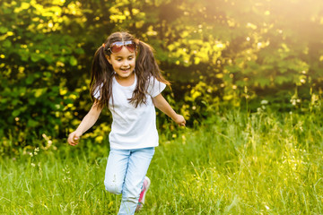 Naklejka na ściany i meble Little girl running on green grass. Beautiful warm summer evening.