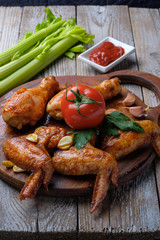 Baked chicken legs and wings lie on the table. Nearby are cherry tomatoes, celery, parsley and spices.