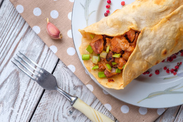 Doner kebab is lying on a white plate. Shawarma with meat, onions, salad lies on a white old wooden table.