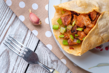 Doner kebab is lying on a white plate. Shawarma with meat, onions, salad lies on a white old wooden table.