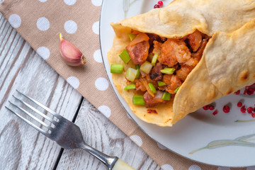 Doner kebab is lying on a white plate. Shawarma with meat, onions, salad lies on a white old wooden table.