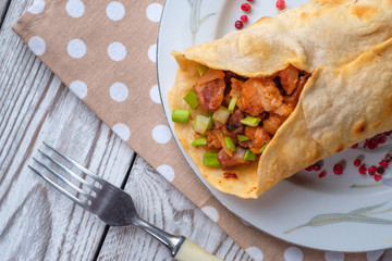 Doner kebab is lying on a white plate. Shawarma with meat, onions, salad lies on a white old wooden table.