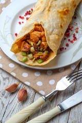 Doner kebab is lying on a white plate. Shawarma with meat, onions, salad lies on a white old wooden table.
