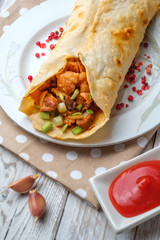 Doner kebab is lying on a white plate. Shawarma with meat, onions, salad lies on a white old wooden table.