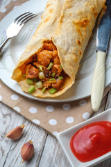 Doner kebab is lying on a white plate. Shawarma with meat, onions, salad lies on a white old wooden table.