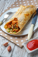 Doner kebab is lying on a white plate. Shawarma with meat, onions, salad lies on a white old wooden table.