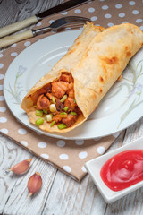 Doner kebab is lying on a white plate. Shawarma with meat, onions, salad lies on a white old wooden table.
