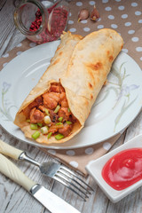 Doner kebab is lying on a white plate. Shawarma with meat, onions, salad lies on a white old wooden table.