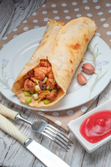 Doner kebab is lying on a white plate. Shawarma with meat, onions, salad lies on a white old wooden table.