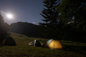 Fototapeta na wymiar A tent glows under a night sky full of stars.
