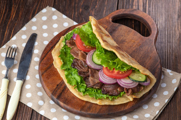 Delicious fresh homemade sandwich with chicken burspit roasted meat, tomato, onions and lettuce on wooden board on dark wooden table. Doner kebab. Healthy food concept.